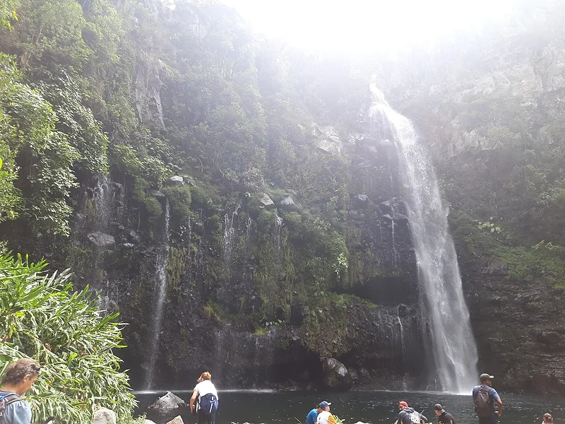 Une cascade au pied d'un rempart couvert de verdure, des randonneurs au bord du bassin