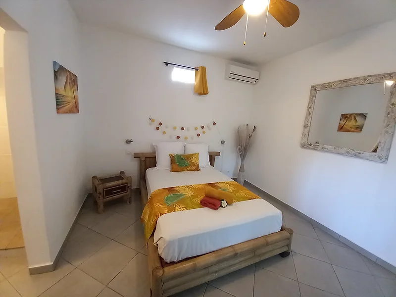 Chambre lumineuse au lit en bois, linge jaune et ventilateur au plafond