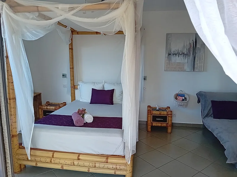 Chambre au lit en bambou avec voilages blancs et coussins violets